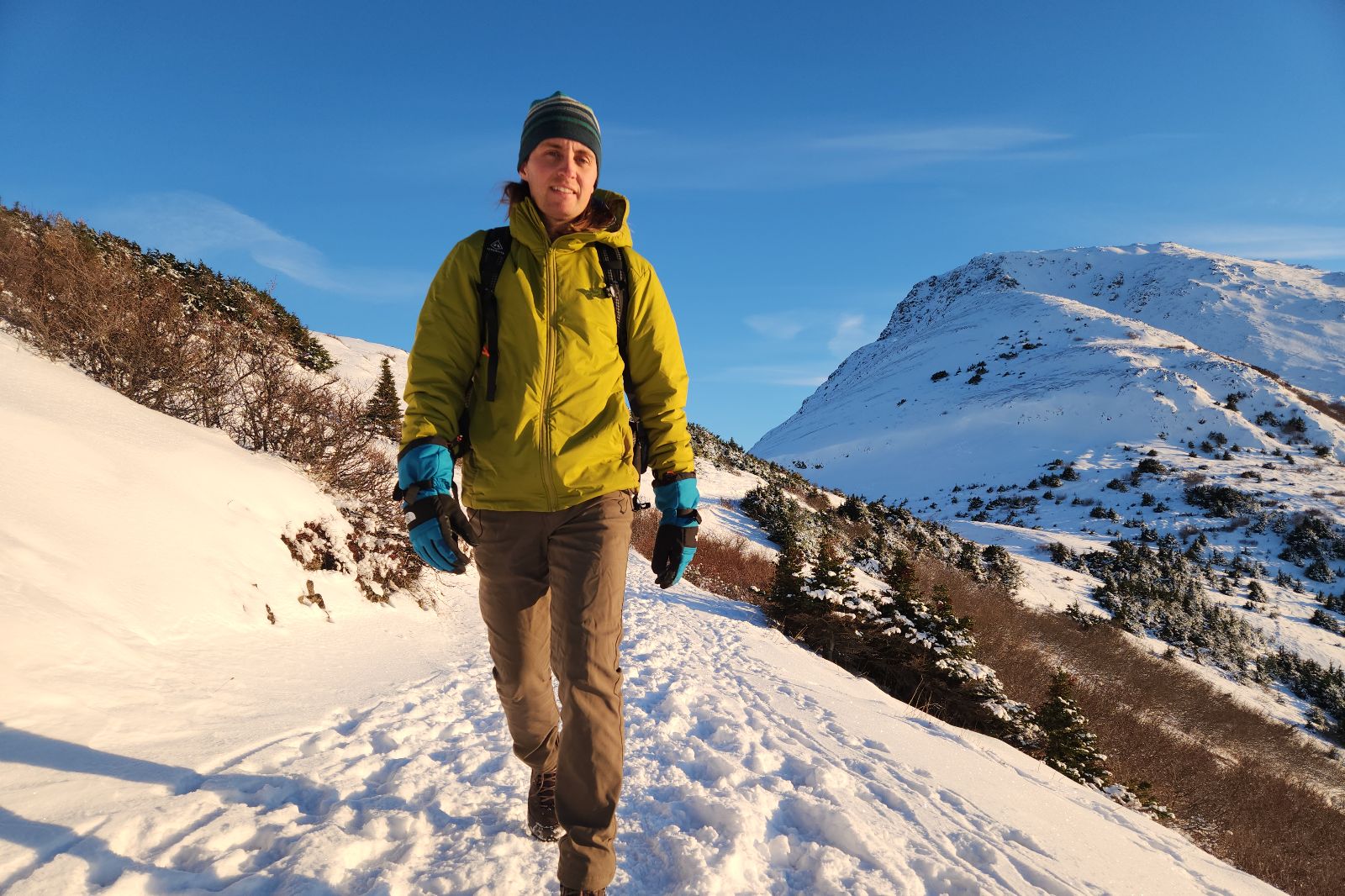 A man hikes in the snowy alpine while wearing a green jacket and blue gloves.