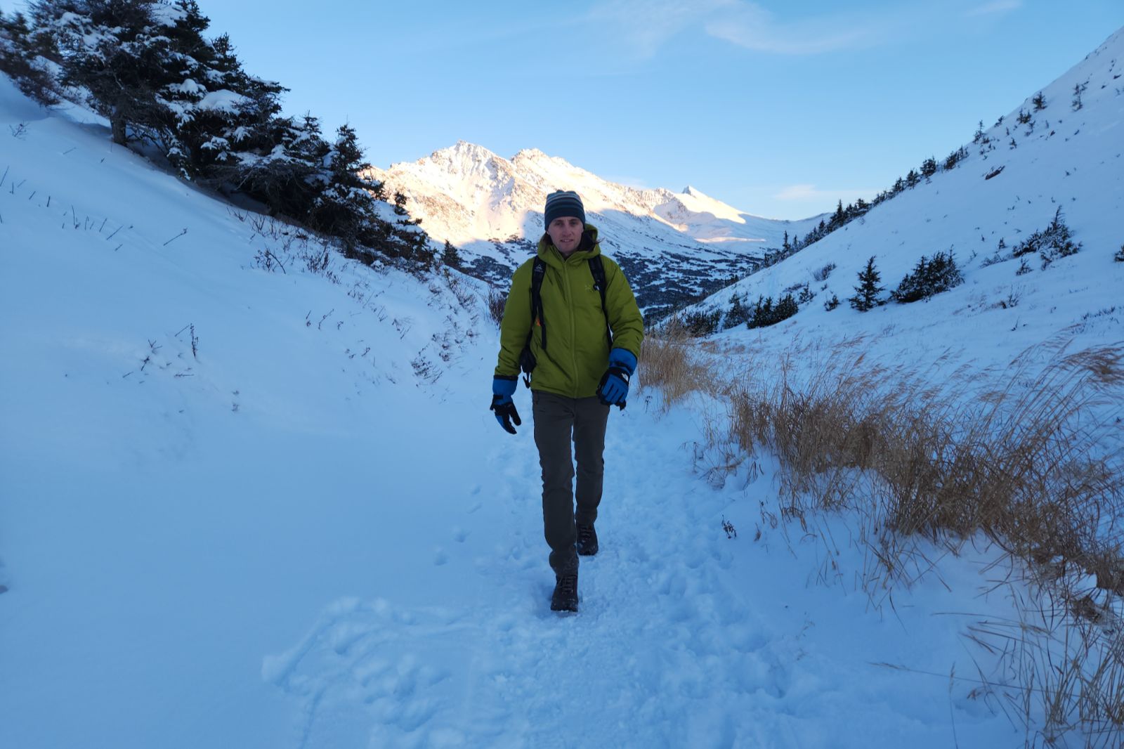 A man hikes through a snowy valley wearing a green jacket.