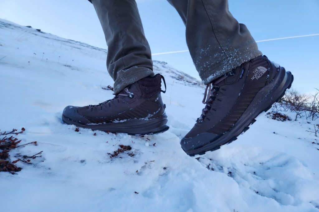 A pair of winter boots walks up a snowy hill.