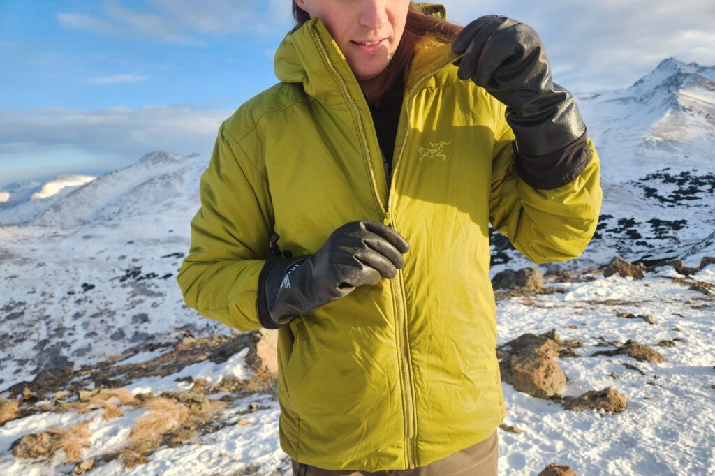 A man zips his jacket while wearing black rubber gloves.