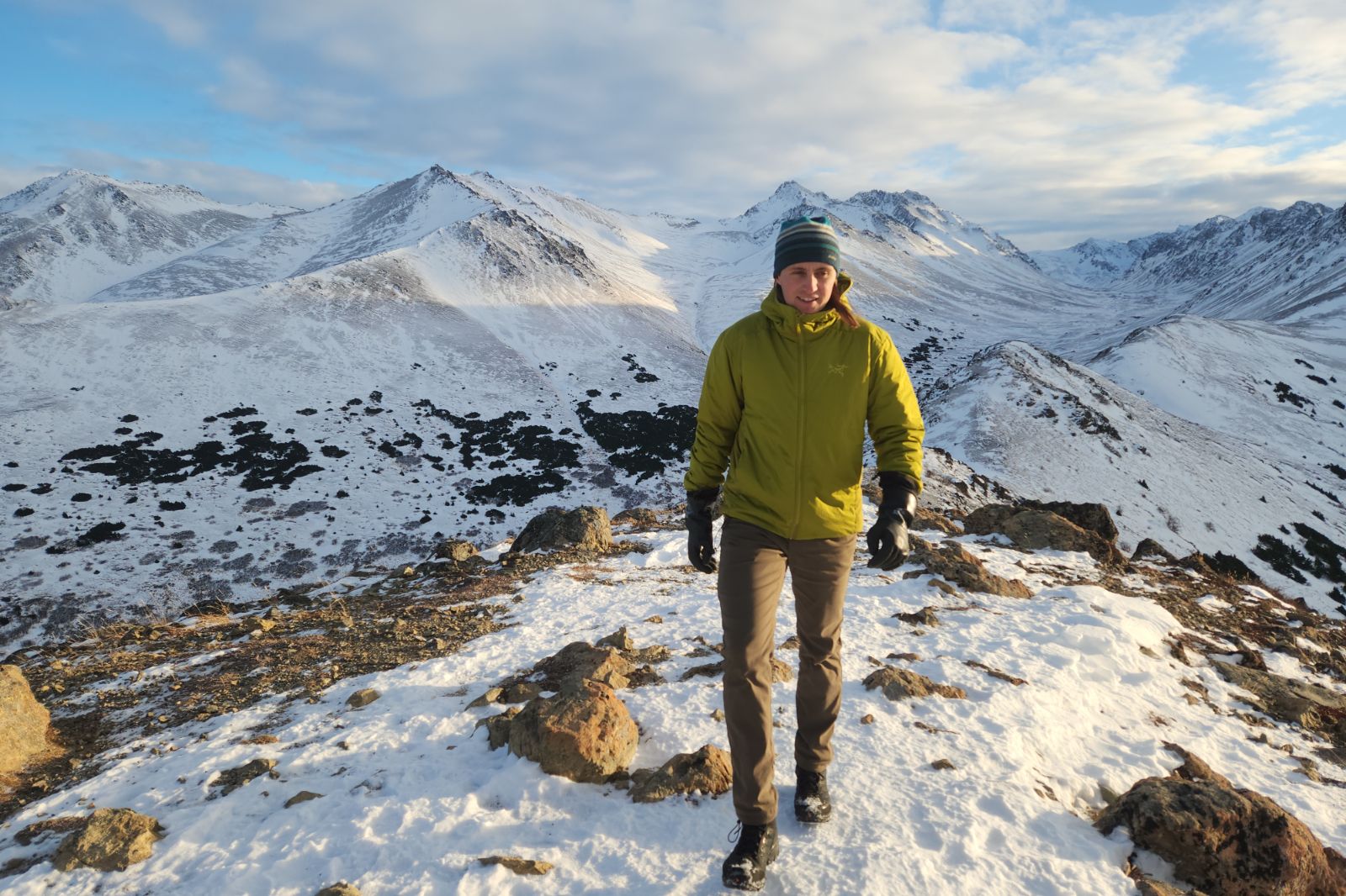 A man hikes on a snowy ridgeline wearing a green jacket.