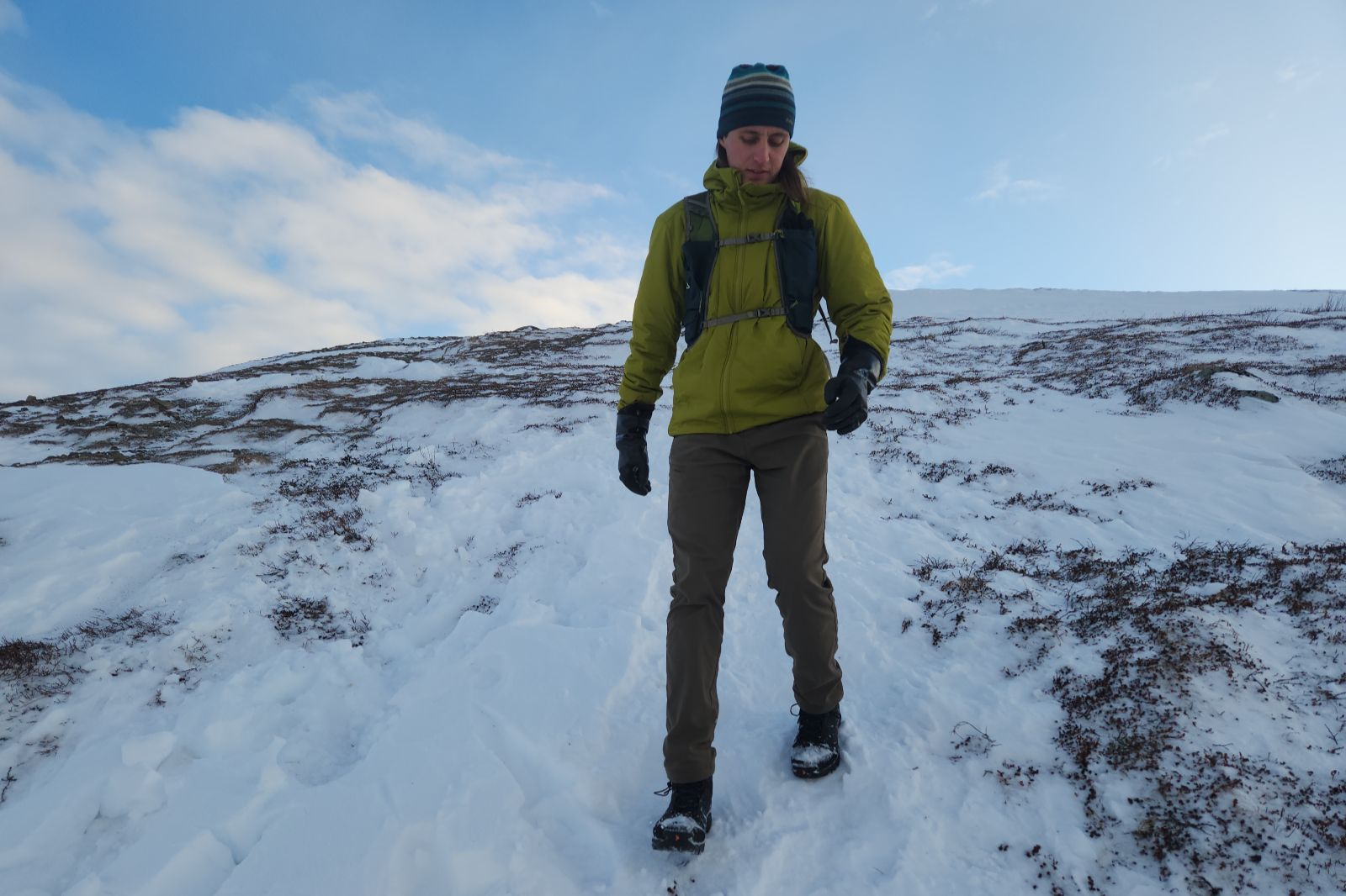 A man hikes down a snowy hill in the alpine wearing black rubber gloves.
