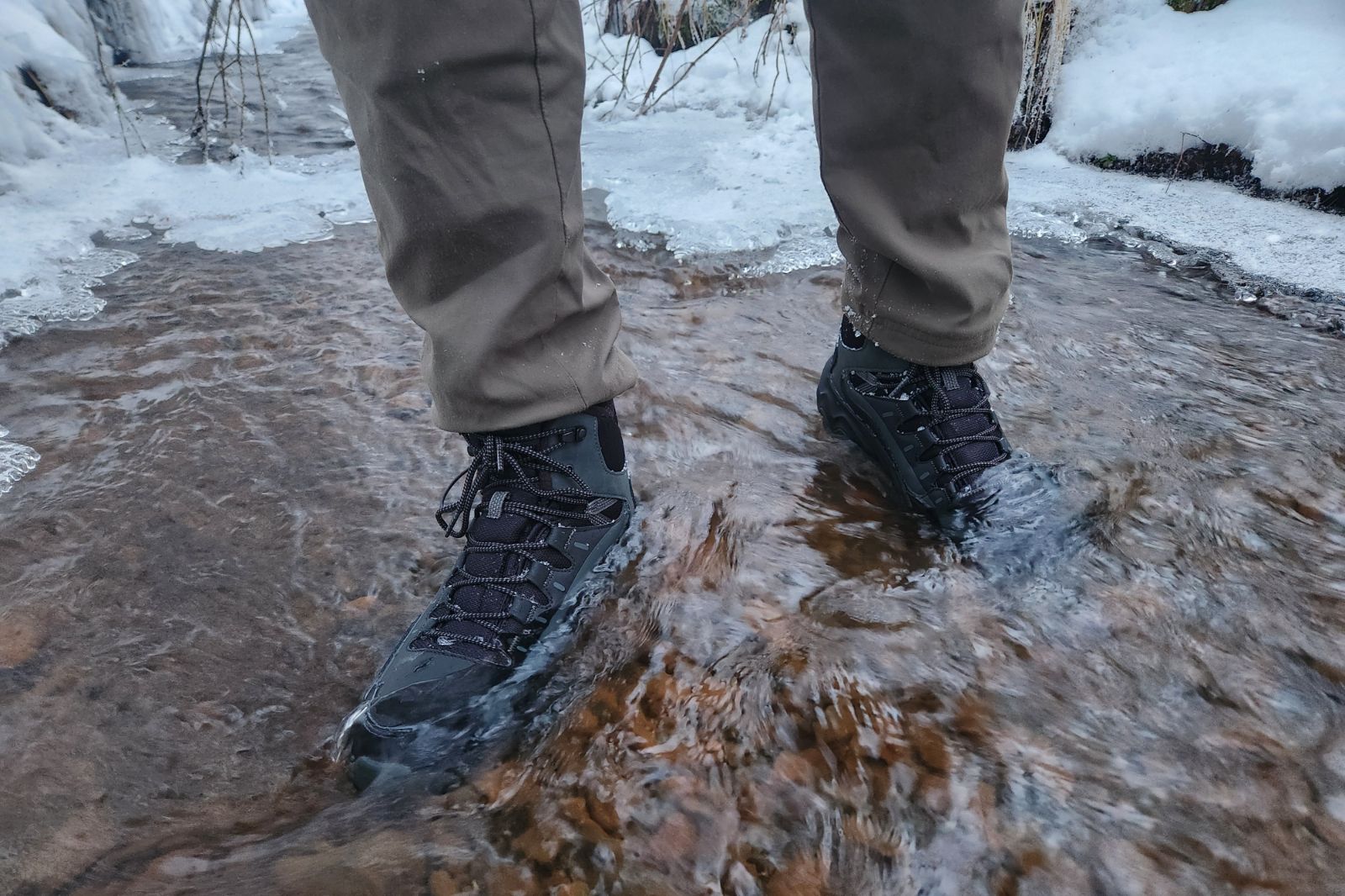A closeup of winter boots standing in an icy creek