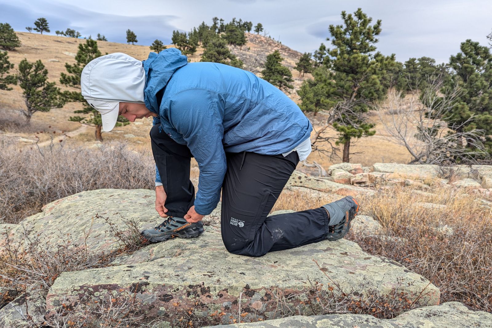 Kneeling a tying a show in the Mountain Hardware Stretch Ozonic rain pants.