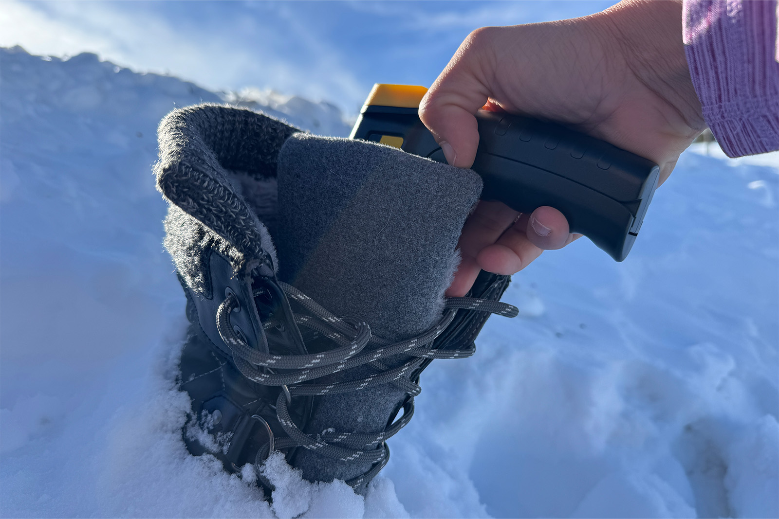 Close up of a hand pointing an infrared thermometer down the inside of a Dream Pairs boot. There is snow in the background.