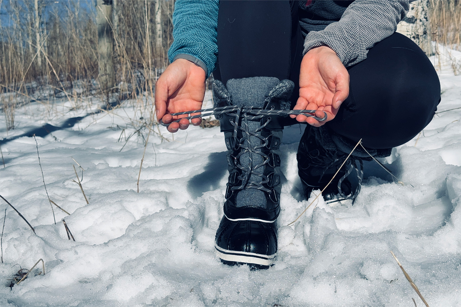 Close up photo showing some hands tying the laces on the Dream Pairs boots. There is snow on the ground and trees in the background.