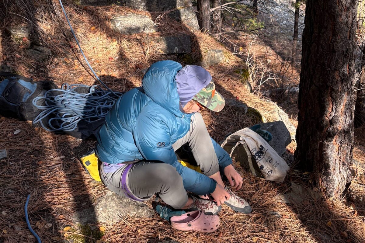 woman putting climbing shoes on while sitting on the ground