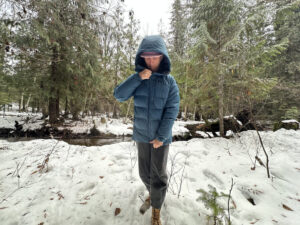 women in a snowy forest near a small creek zipping up a winter down jacket