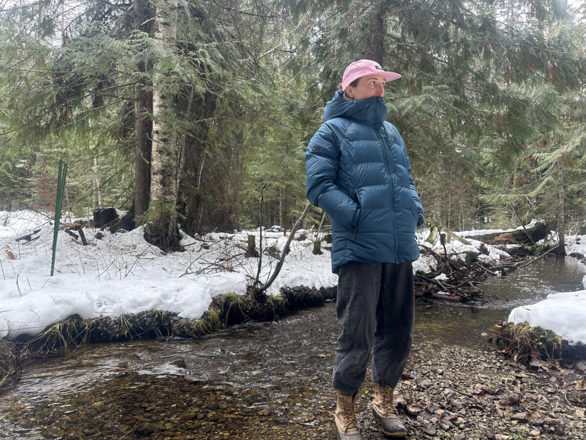 woman standing next to a winter creek with her chin tucked into a down jacket