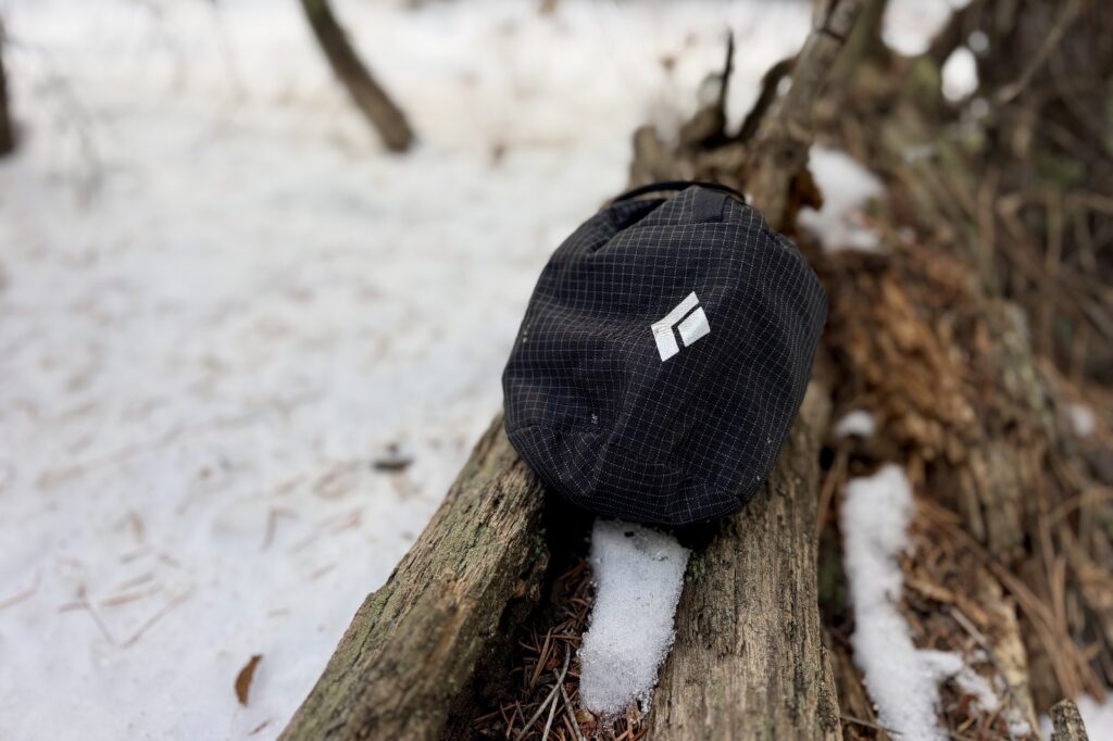 a stuff sack with ice cleats sits on a log in a snowy environment