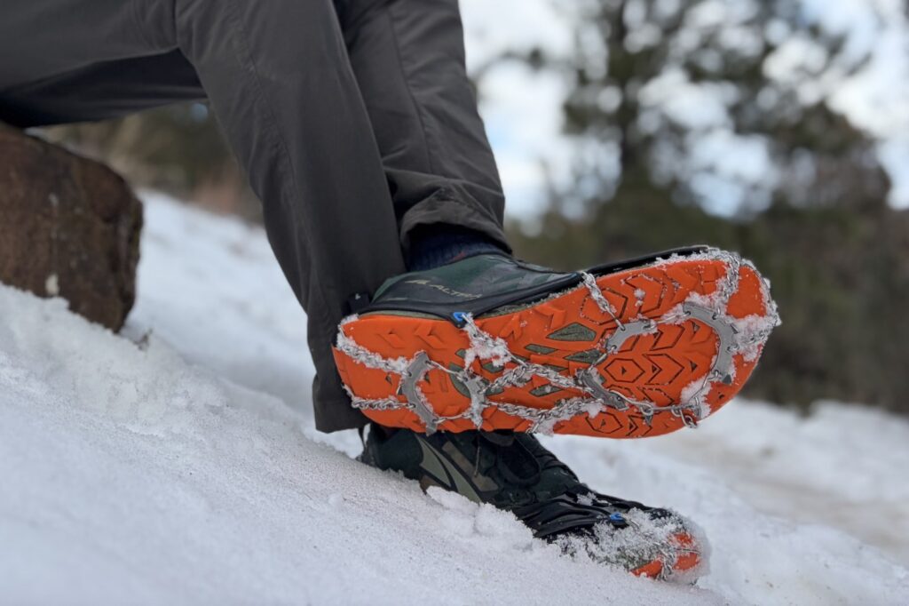 a hiker shoes the bottom of one shoe with ice cleats attached
