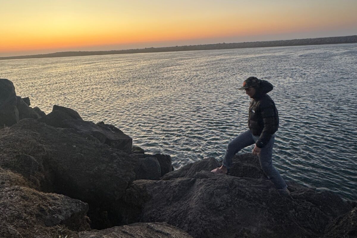 women walking on boulders at sunset in a down jacket