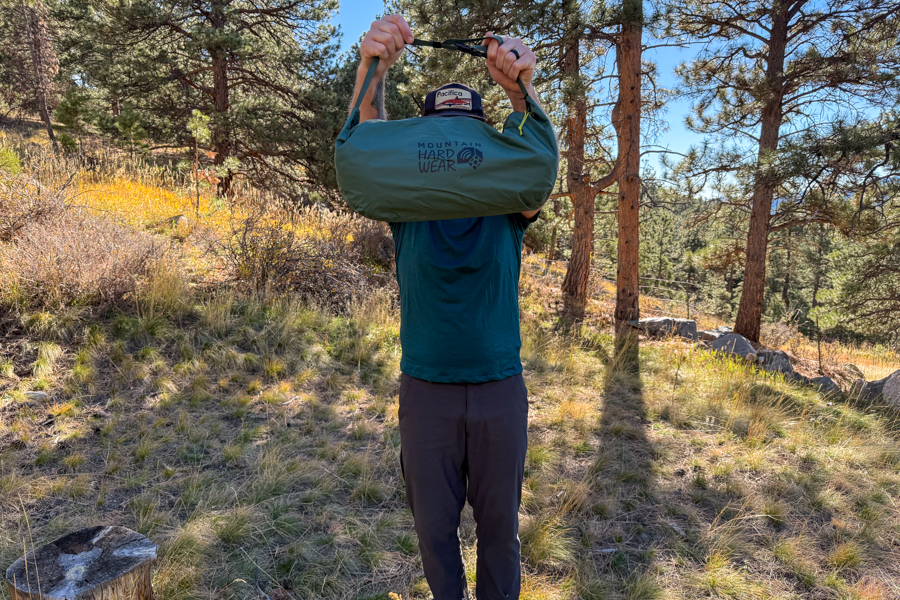 A person holding the packed Mountain Hardwear Mineral King 2 All Season tent overhead in a green stuff sack, standing in a sunny forest meadow.