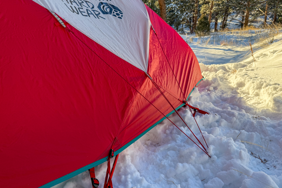 Close-up of the Trango 2’s red fly with taut red guylines staked into the snow, highlighting the tent’s anchoring system.