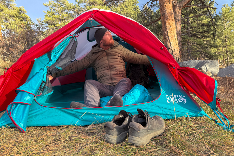 A person sitting in the open doorway of the Trango 2, reaching to adjust the interior door, with shoes placed outside on dry grass.
