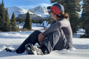 A person wearing the Toundra boots sits in the snow and enjoys the view of a mountain.