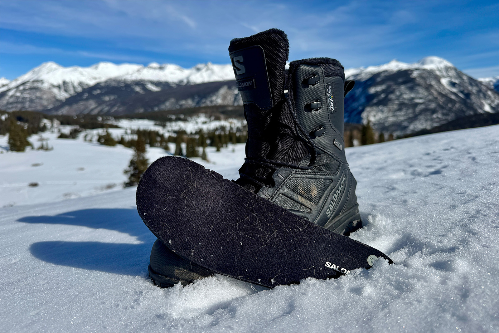 Close up of a Toundra boot with the insole sitting in the snow next to it. There are mountains in the background.