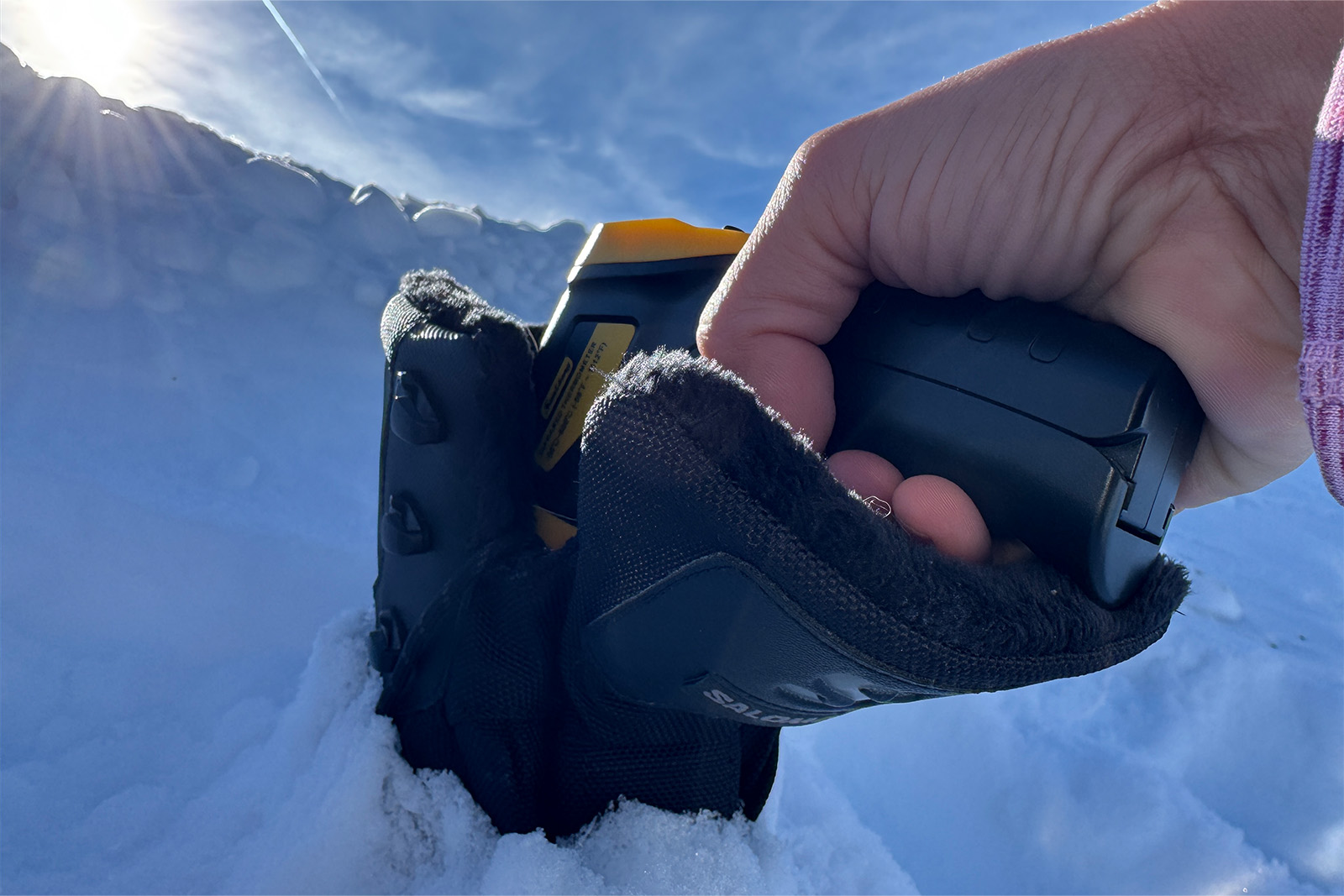 Close up of a hand pointing an infrared thermometer down the inside of a Toundra boot. There is snow in the background.