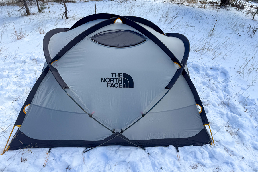 The North Face Mountain 25 tent set up in snow with the fly removed, showing the gray tent body, black reinforcement panels, and crossed pole structure.