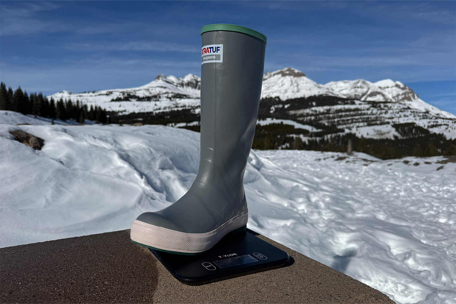 An Xtratuf boot sits on a kitchen scale. There are mountains in the background.