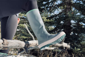 Close up of an Xtratuf boot as a person steps over a branch in a forest.