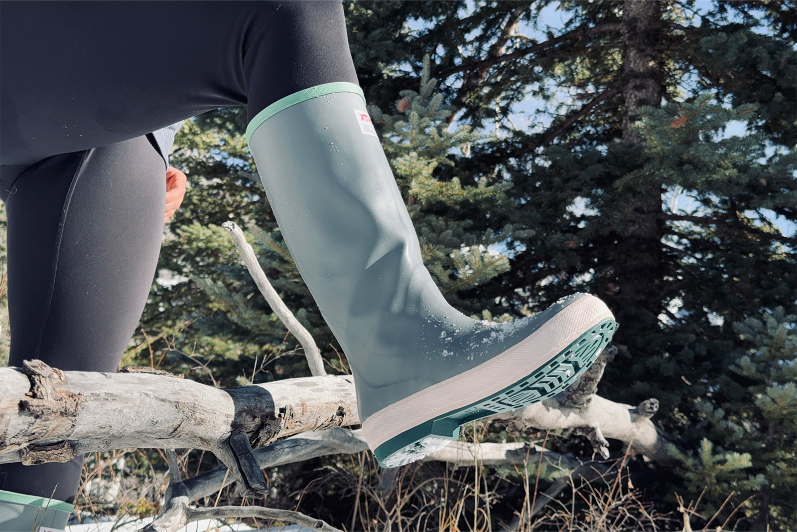 Close up of an Xtratuf boot as a person steps over a branch in a forest.
