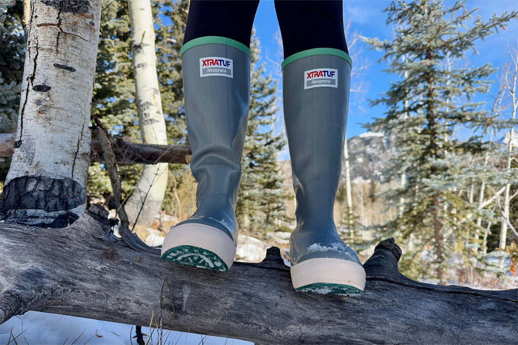 A close of a person wearing Xtratuf boots who is standing balanced on a log.