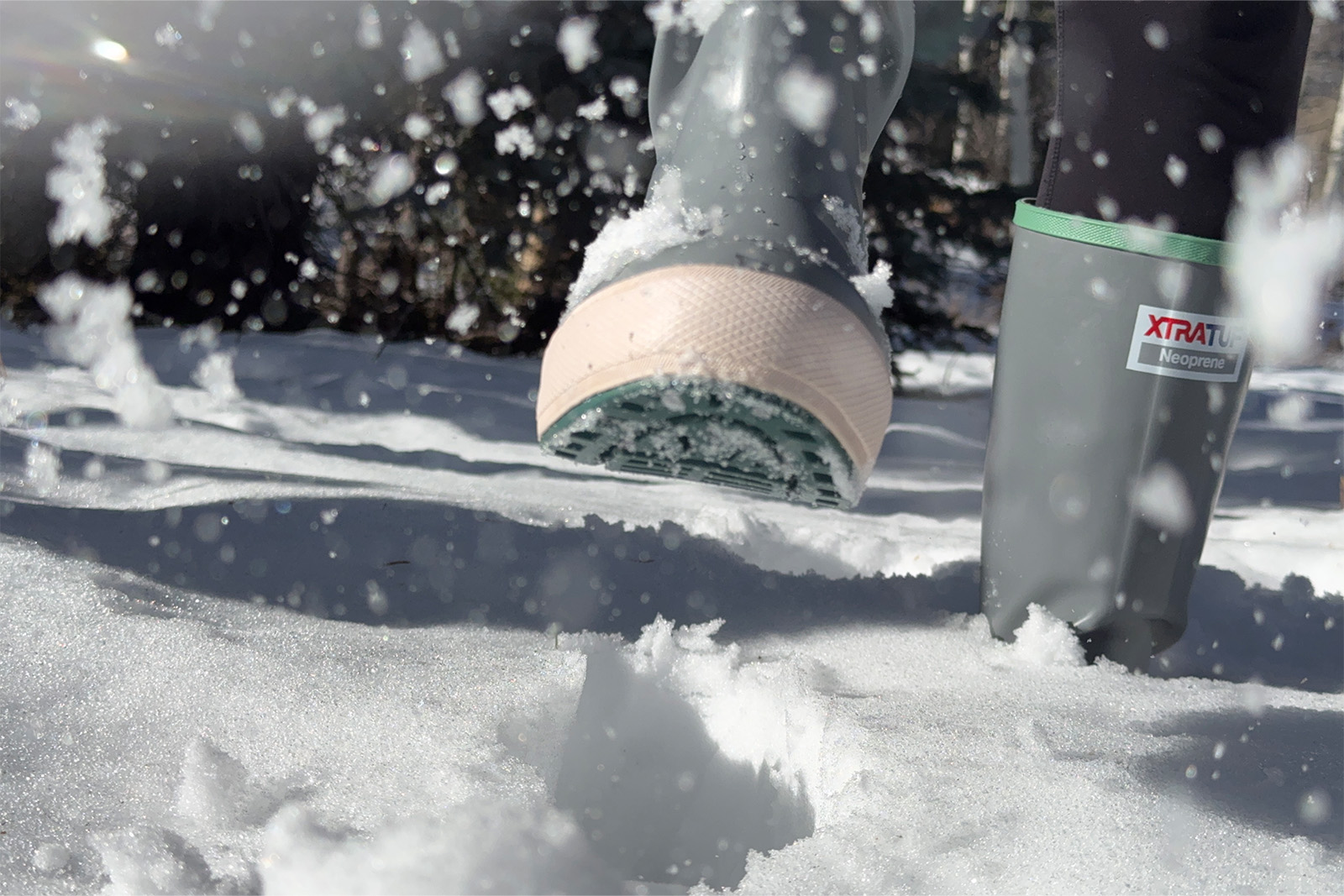 Close up of a person wearing Xtratuf boots kicking snow at the camera.