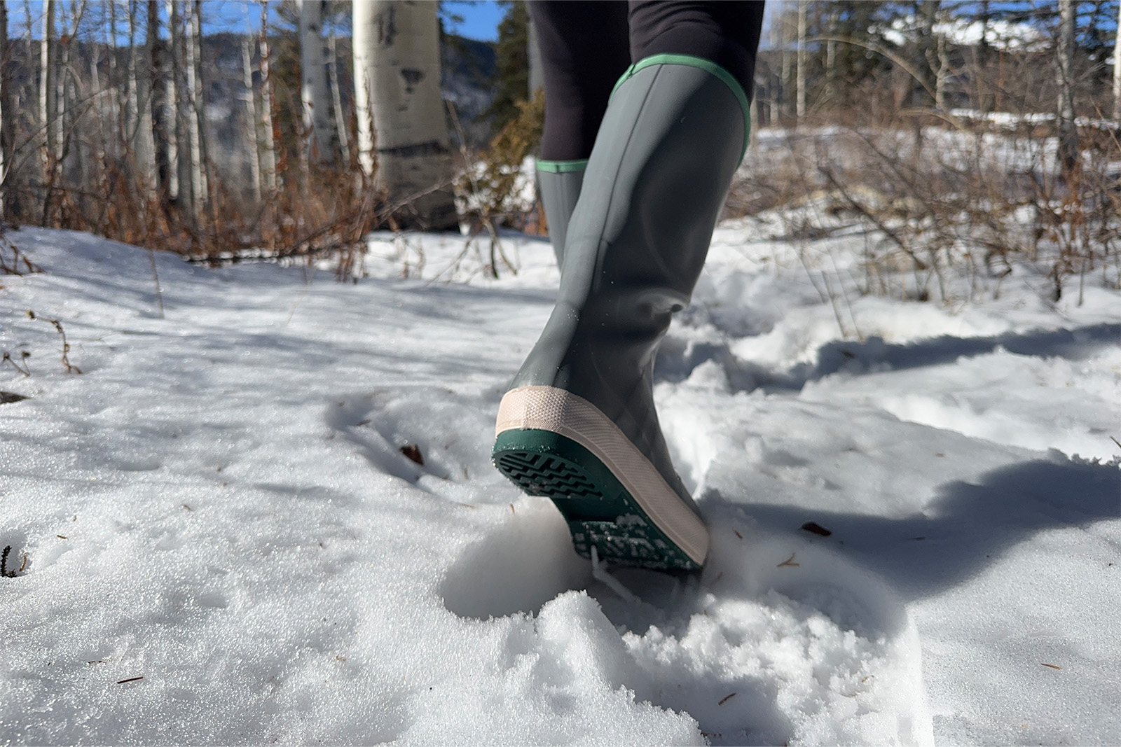 Close up of the tread on an Xtratuf boot as a person walks away from the camera in the snow.