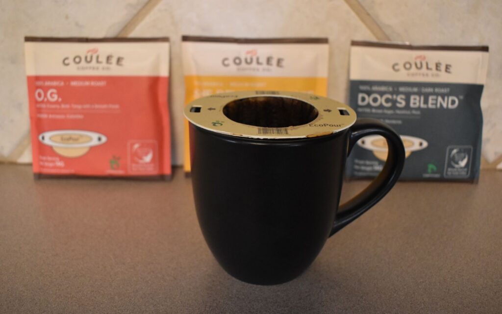 An EcoPour filter on a mug of coffee with freshness packs of Coulee Coffee blurred in the background