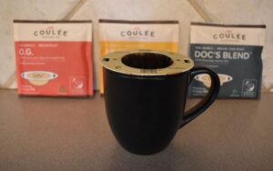 An EcoPour filter on a mug of coffee with freshness packs of Coulee Coffee blurred in the background
