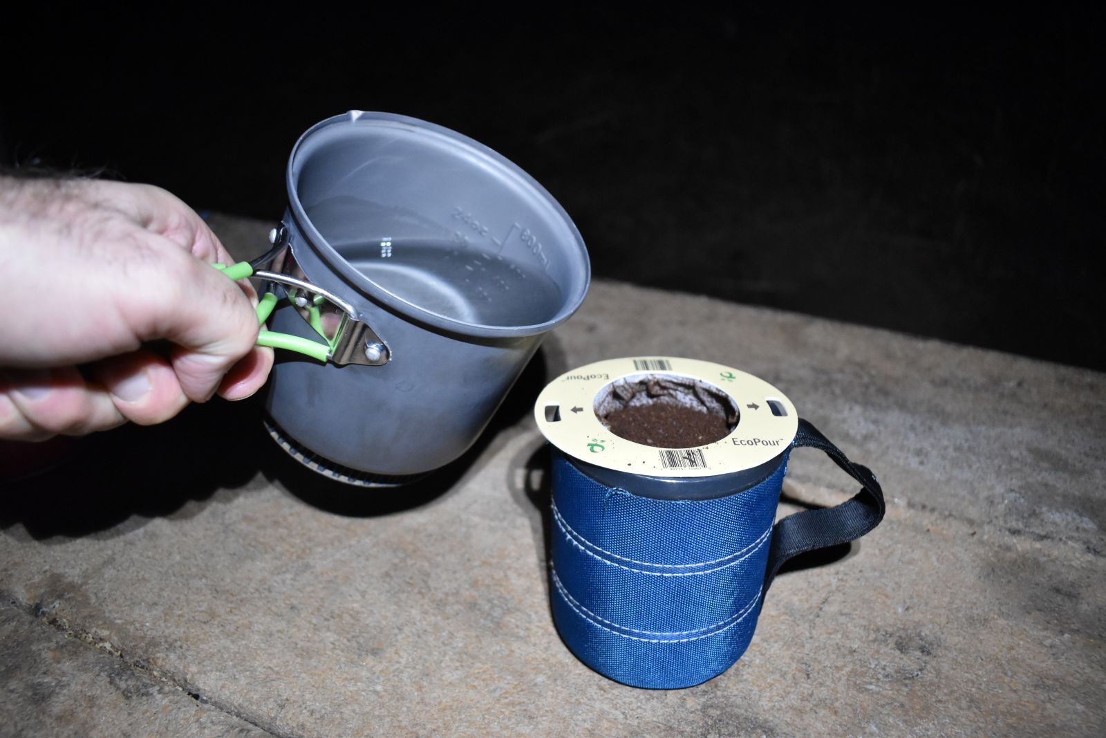 A hiker pours near-boiling water from a camp pot into an EcoPour filter on a blue coffee mug