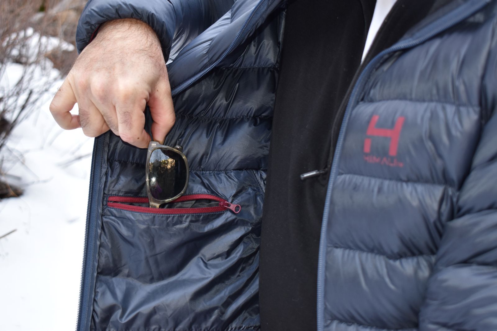 A hike drops a pair of sunglasses into the internal chest pocket of the HIMALI Accelerator down jacket