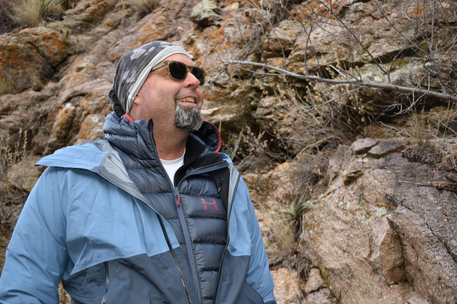 A male hiker with a rain jacket half opened to show the HIMALI Down Accelerator layered underneath