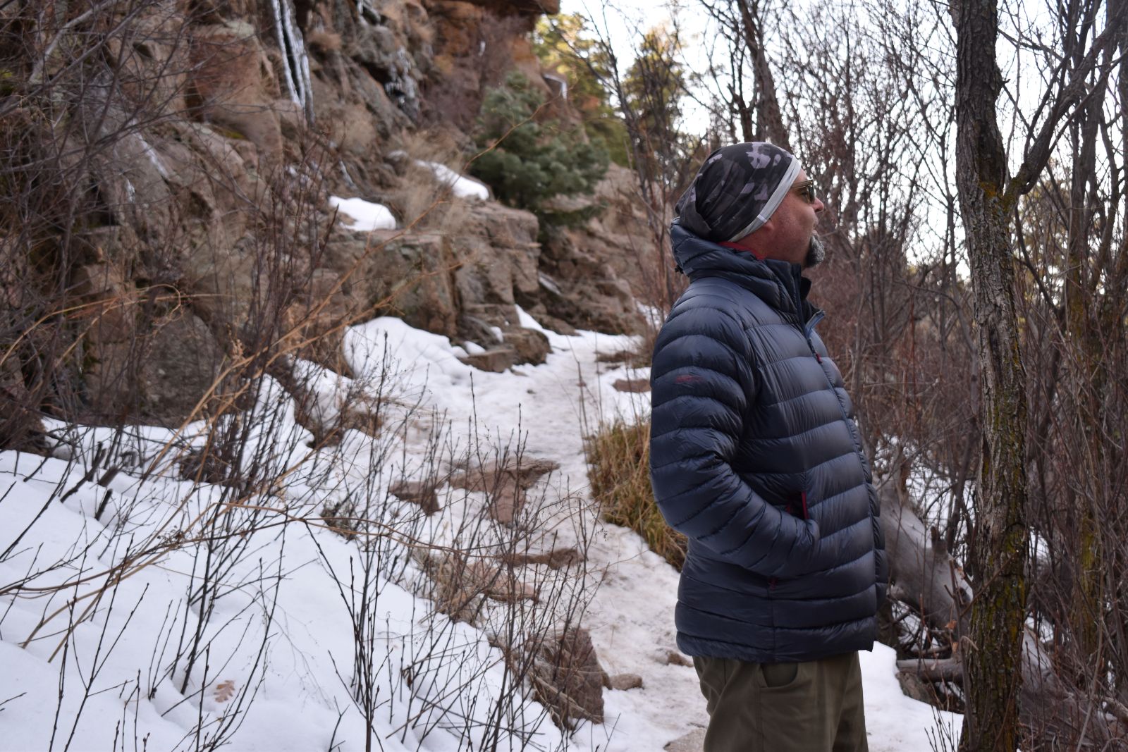 A hiker stands on a snow trail wearing a blue HIMALI Accelerator down jacket