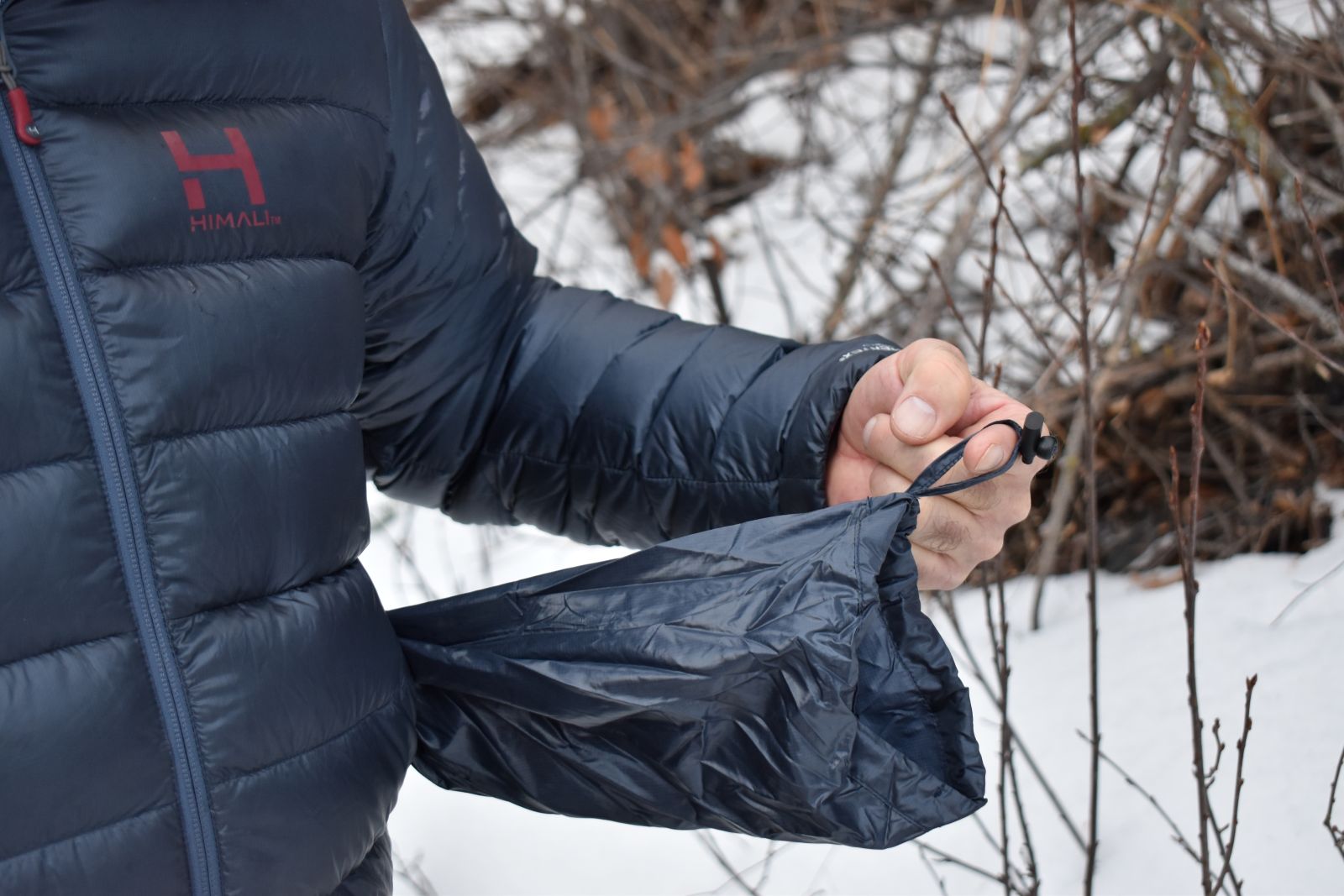 A hiker pulls the attached stuff sack out of the front pocket of the HIMALI Accelerator jacket