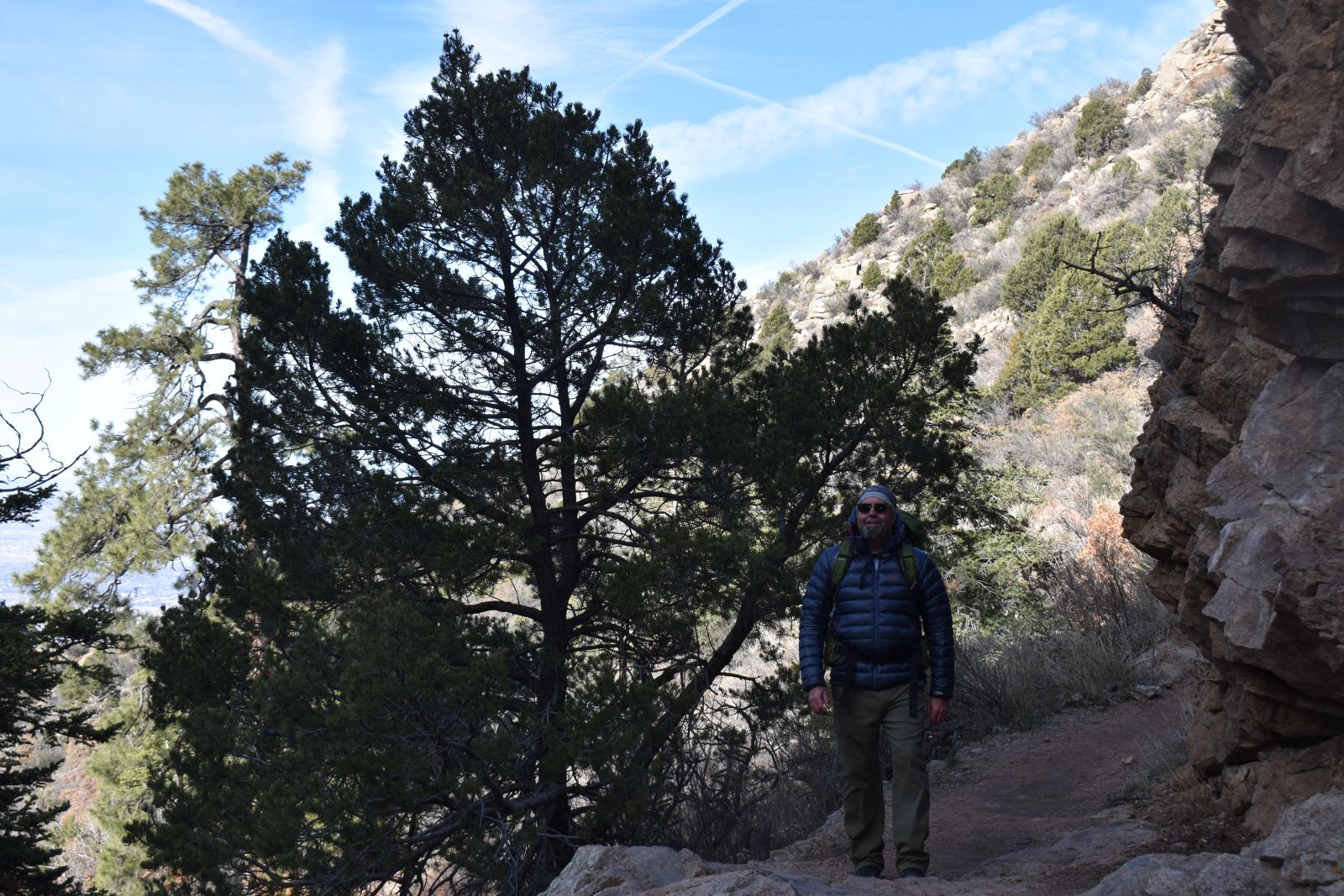 A hiker wears a blue HIMALI Accelerator down jacket under a backpack while hiking up a desert mountain in winter