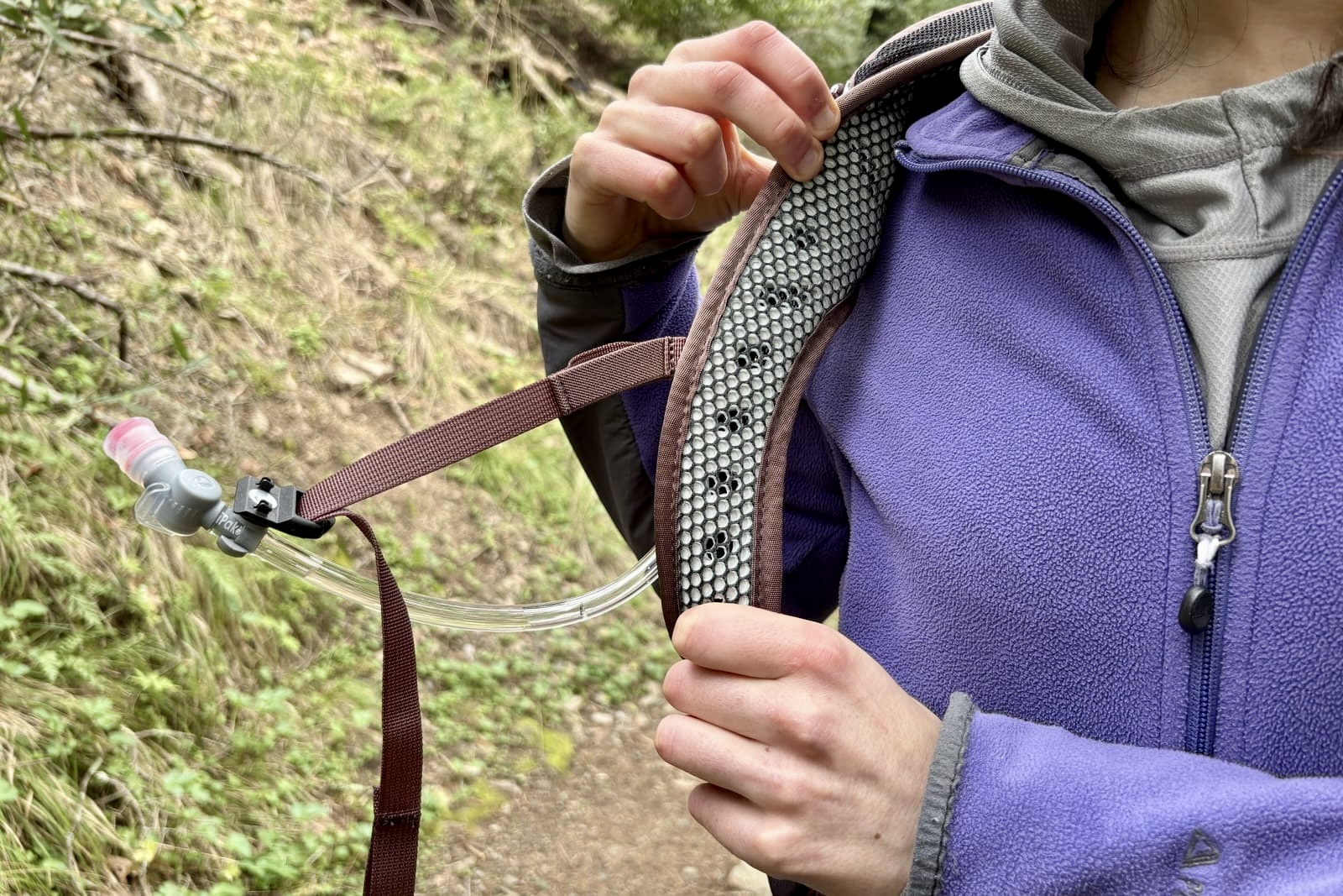 A woman shows the padding in the shoulder straps of her backpack.
