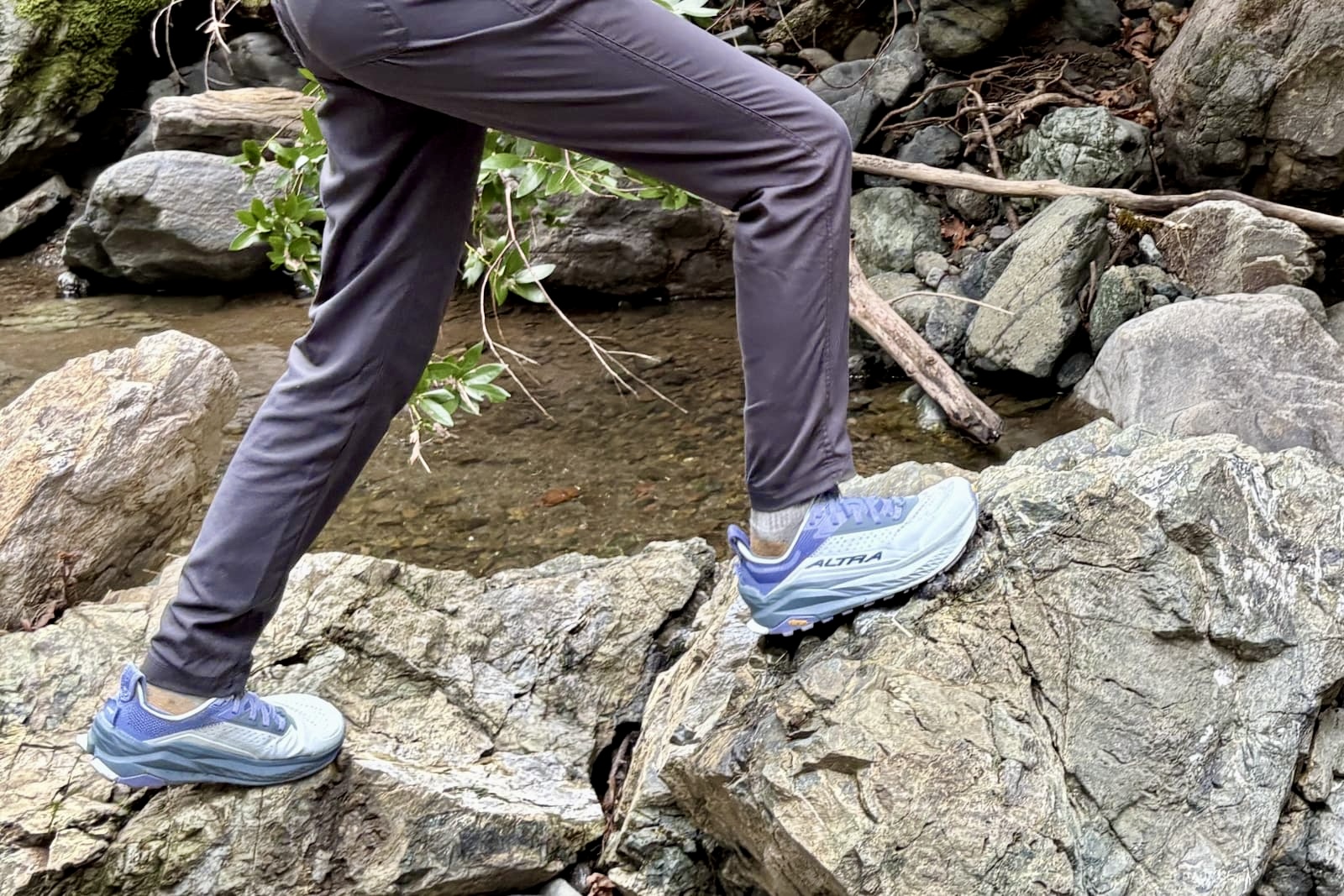 A woman steps across rocks to cross a creek.
