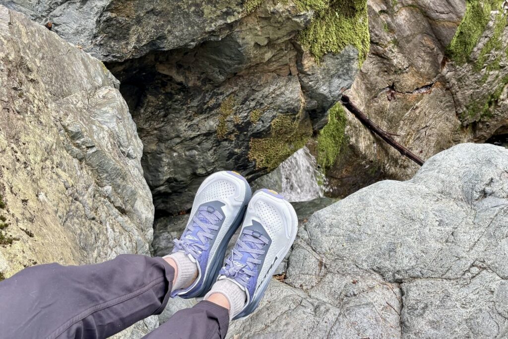 A closeup of a woman's pair of hiking shoes as she sits on a ledge.