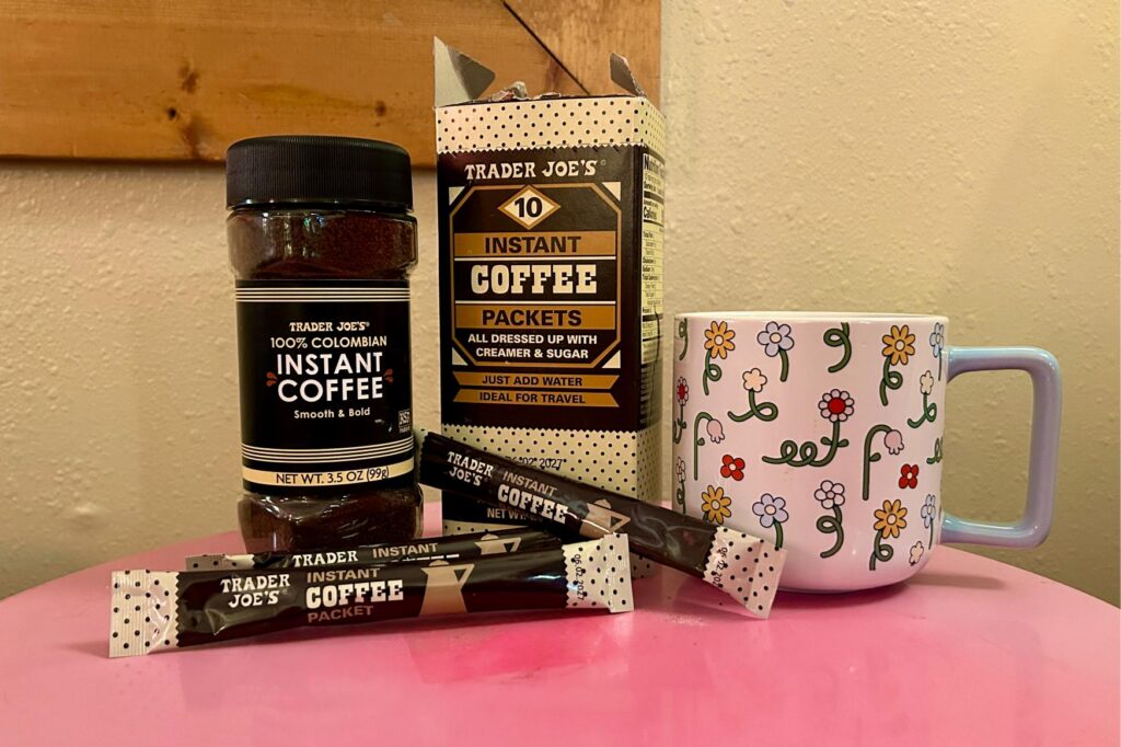 Up-close image of both trader joe's coffee in bulk and packets next to a mug on a pink table.