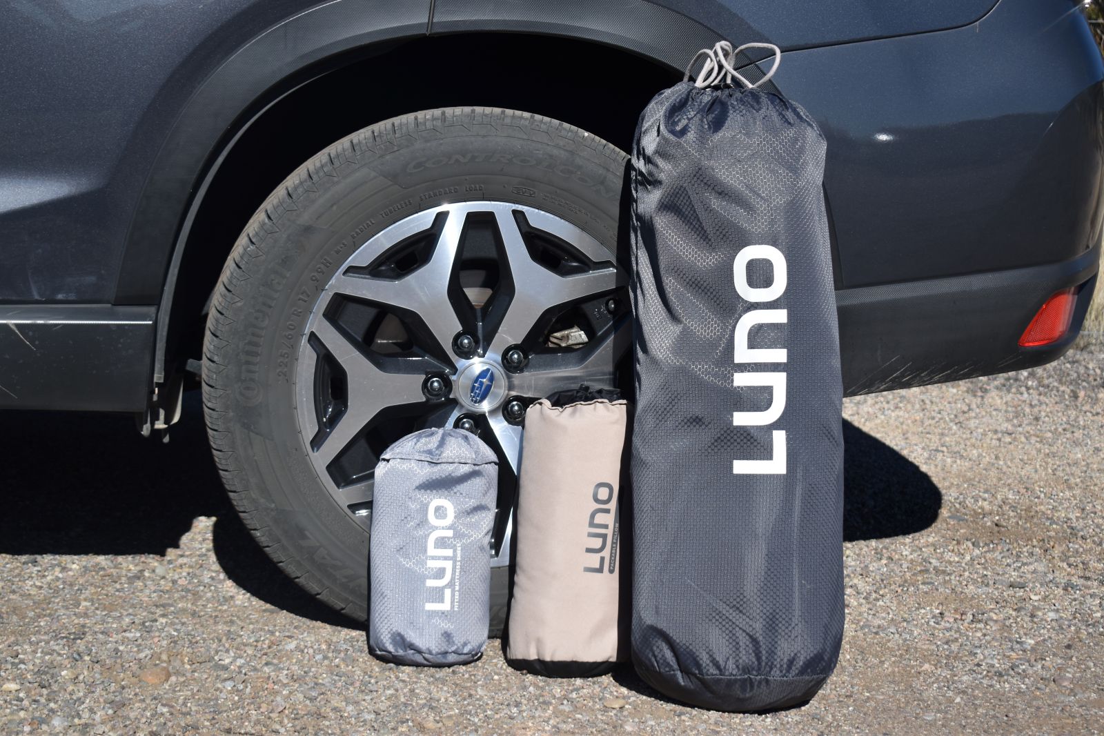 Three Luno stuff sacks lined up against the tire of an SUV.