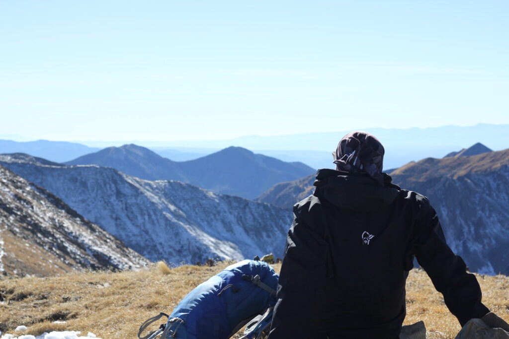 A rear view of a hiking reclining on a mountain ridge at 12,000 feet in the Norrona trollveggen waterproof jacket