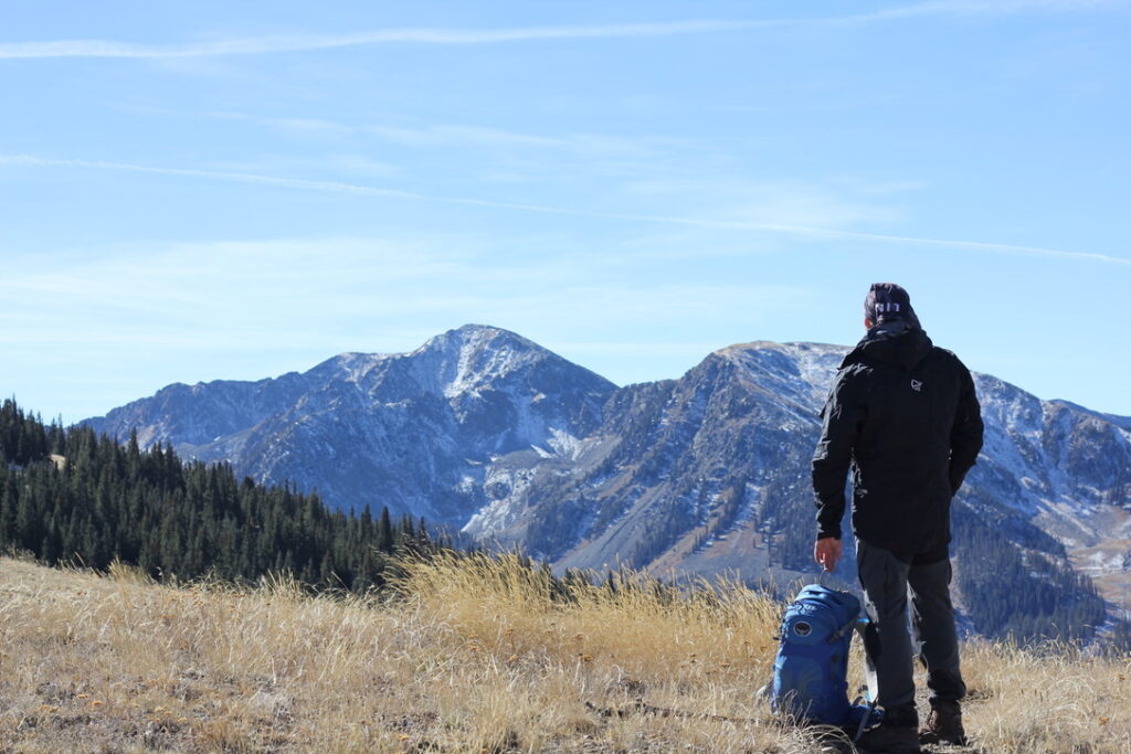 A hiker stands above tree line in a black Norrona trollveggen shell