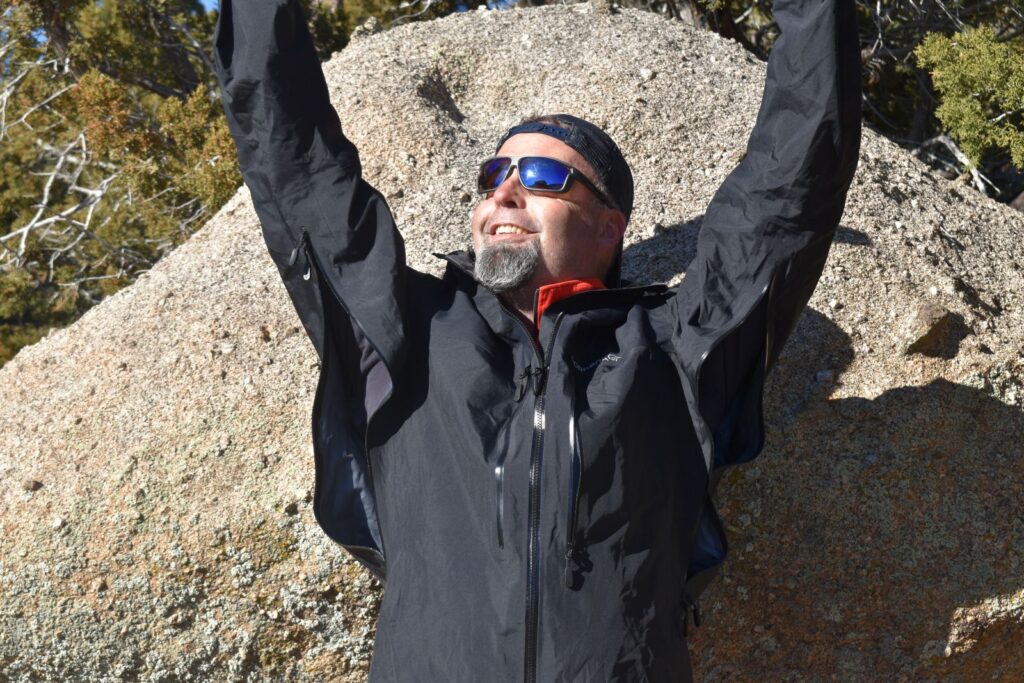 A hiker raises his arms in the Norrona trollveggen jacket to show the extra-long ventilation zippers under the arms
