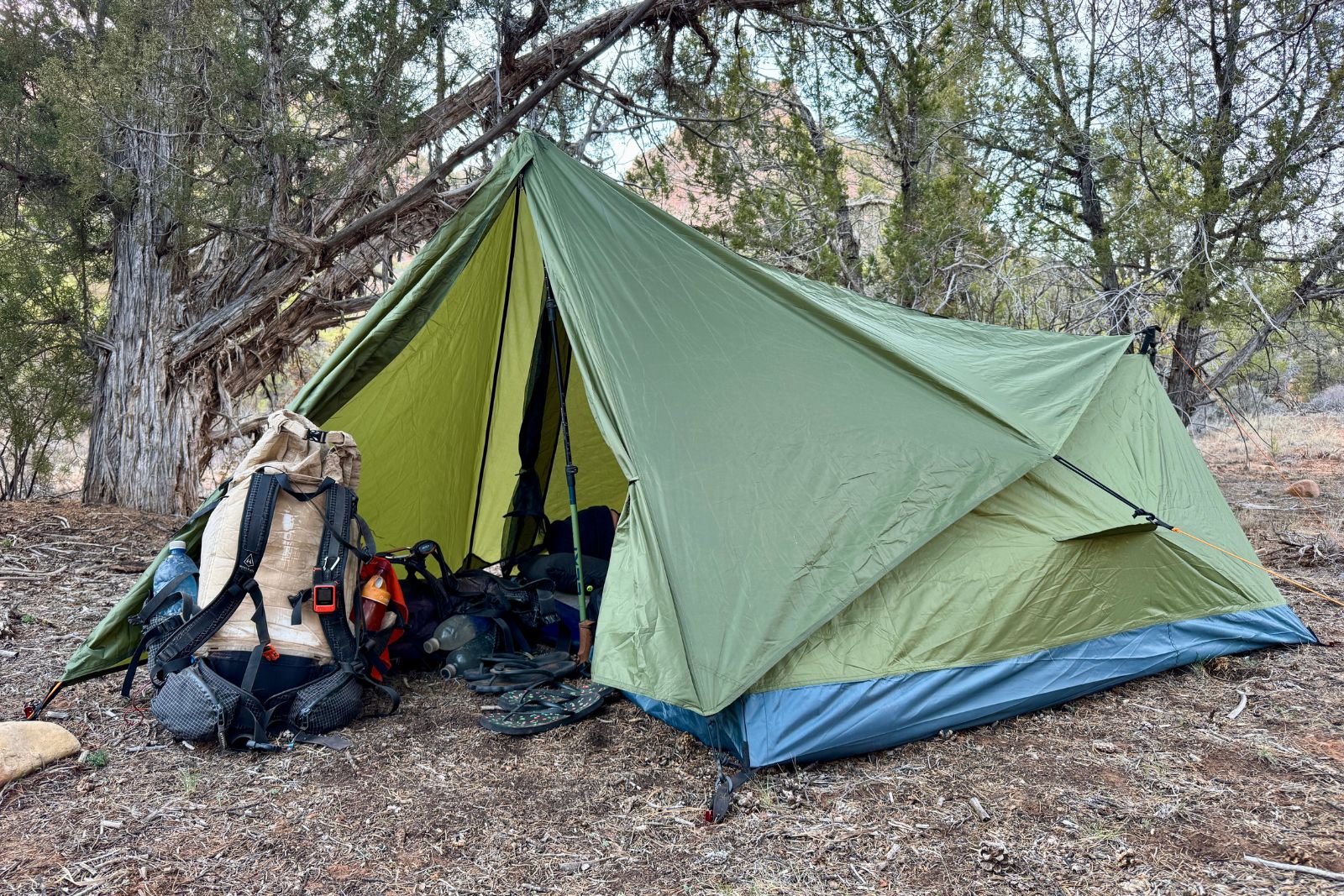 The River Country tent is set up in a pinion-juniper forest with the rain fly on and a backpack propped up in the open vestibule.