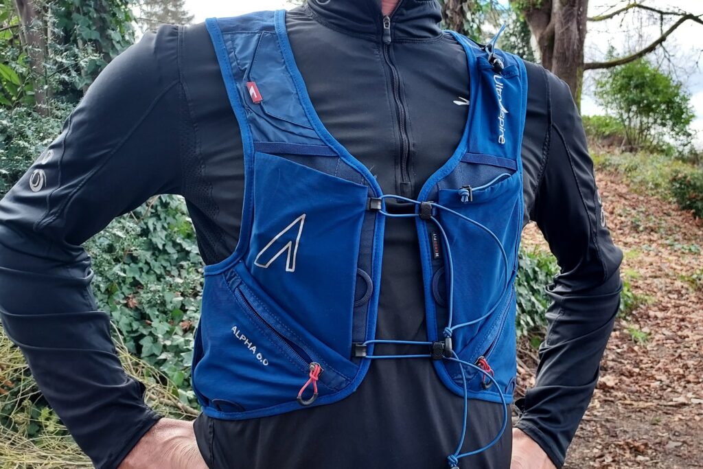 Close-up image of a woman wearing a blue running vest with a forest trail in the background.