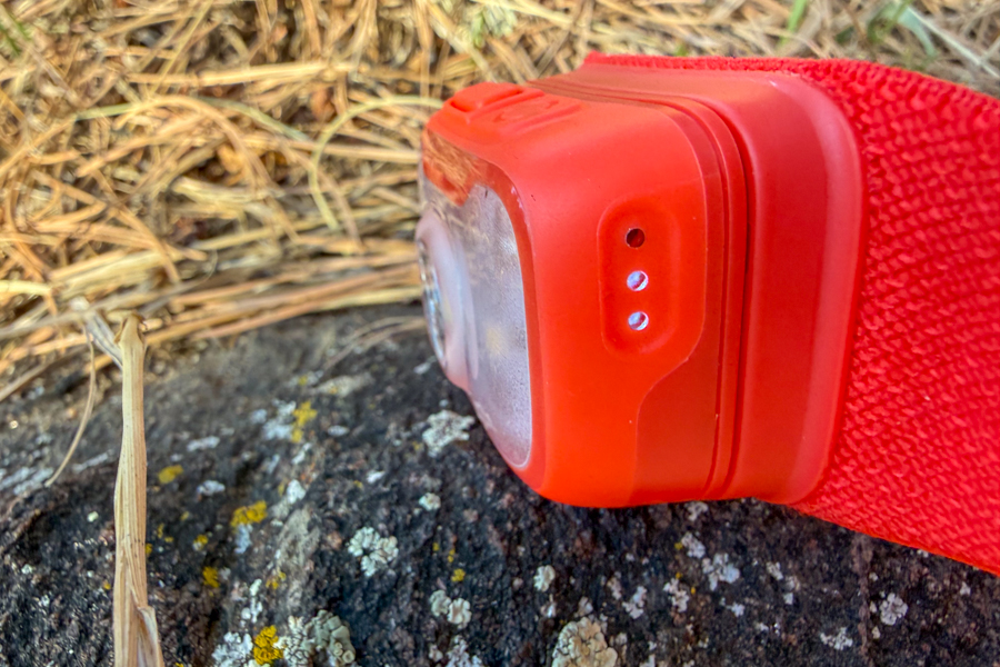 Side view of a red BioLite headlamp on a rock, showing the slim light housing and headband in dry grass.