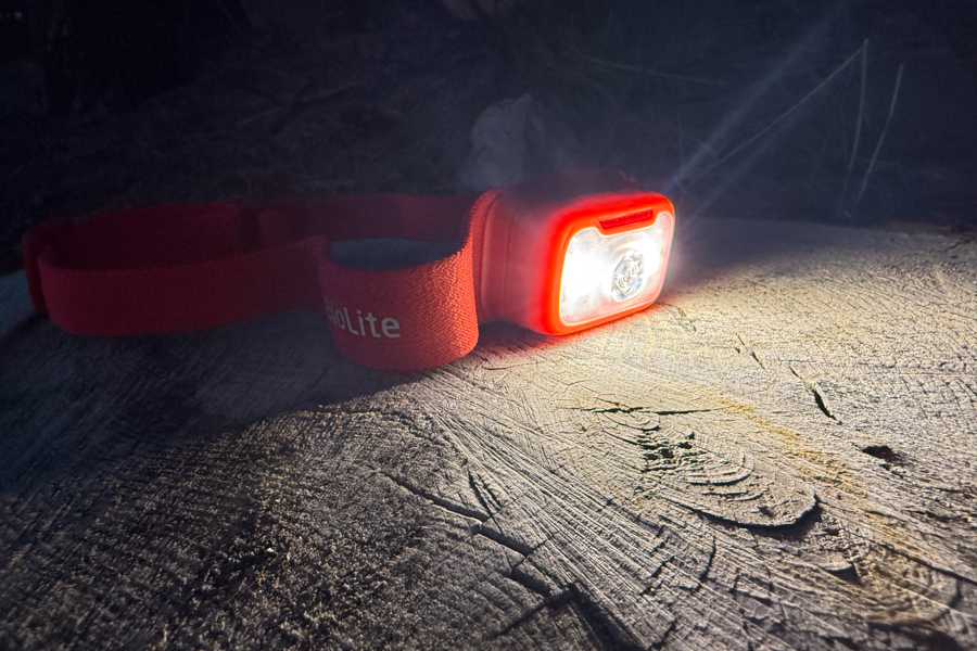 BioLite headlamp resting on a log at night, shining a bright white beam across the wood grain.