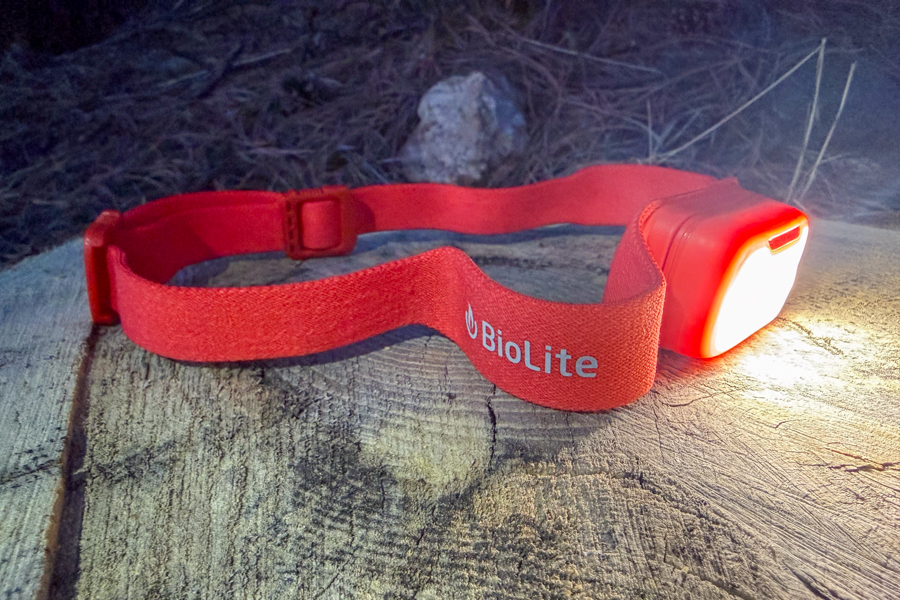 BioLite headlamp on a log with the strap visible, casting a wide beam and lighting up the surface at night.